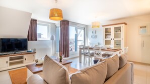 Een moderne woonkamer met een flatscreen televisie, een bank, een eettafel met stoelen en een keuken met kastjes.