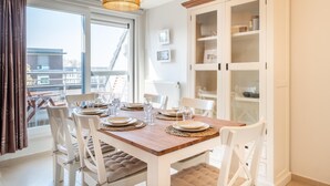 Een eethoek met een houten tafel voor vier personen, witte stoelen en een grote kast met glazen deuren.