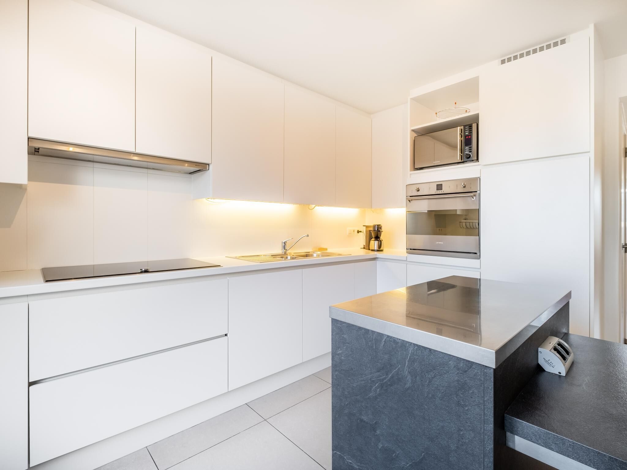 Eine moderne Küche mit weißen Schränken, einem eingebauten Backofen, einer Mikrowelle und einer Kochinsel mit Granitplatte.
