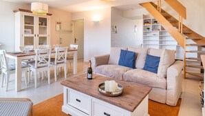 Een moderne woonkamer met een eethoek, een bank, een salontafel en een trap.