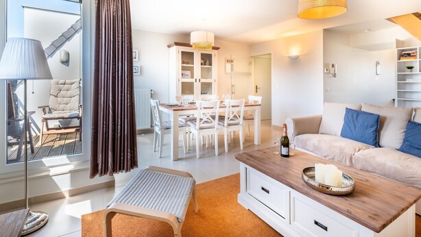 Een moderne woonkamer met een bank, een eettafel en een salontafel. Er is een raam met gordijnen, een lamp en een radiator.