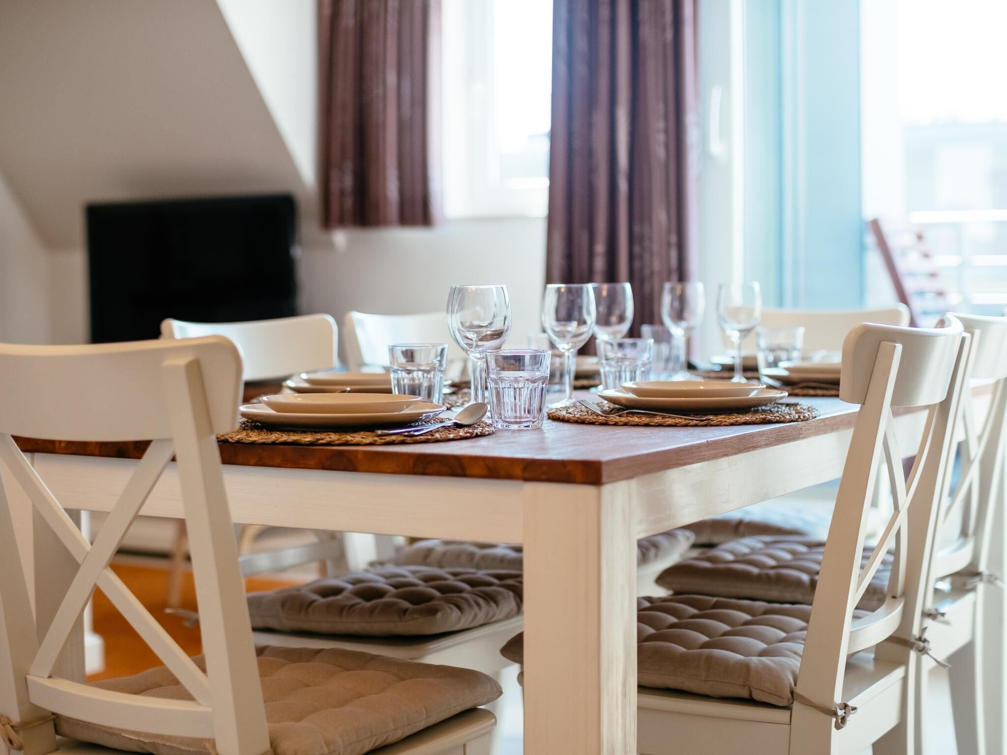 Une table à manger dressée avec des assiettes, des verres et des couverts, entourée de chaises rembourrées.