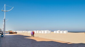 A beach with white beach huts, a paved walkway, and a clear blue sky.