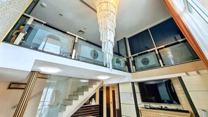 A modern interior with a grand chandelier, a staircase, and a balcony with decorative railings. - Harmony Living Condominium (Bangkok)
