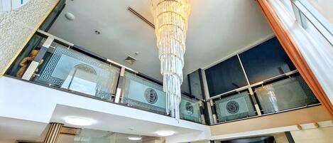 A modern interior with a grand chandelier, a staircase, and a balcony with decorative railings.