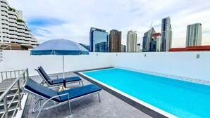 A rooftop swimming pool with lounge chairs and an umbrella, surrounded by a city skyline. - Harmony Living Condominium (Bangkok)