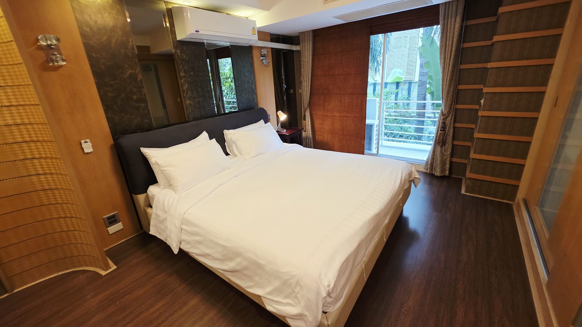 A hotel room with a large bed, a wooden door, and a view of the outdoors.