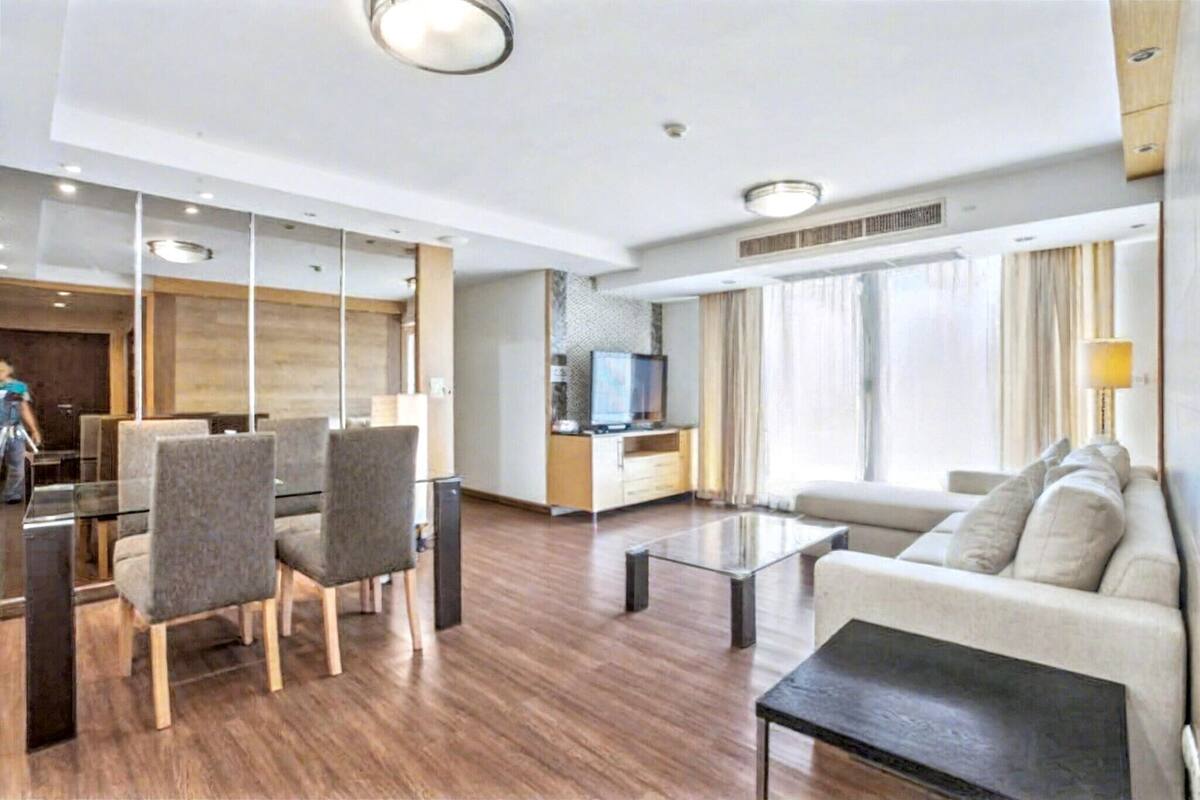 A modern hotel room with a dining area, a sofa, a TV, and a large window.