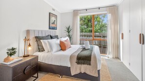 Een moderne slaapkamer met een bed, nachtkastje, lamp en uitzicht op groen.