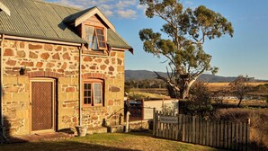 A stone building with a metal roof, a wooden door, and a window with a wooden frame. - Blacksmith's Cottage at Lisdillon Estate (Little Swanport)