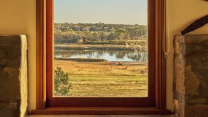 A room with a large window overlooking a landscape with a body of water and trees. - Blacksmith's Cottage at Lisdillon Estate (Little Swanport)
