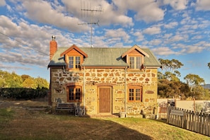 Uma casa de pedra com telhado de metal, chaminé e cerca de madeira.