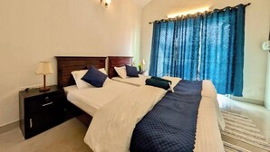 A hotel room with two beds, a nightstand, a lamp, and a window with curtains.