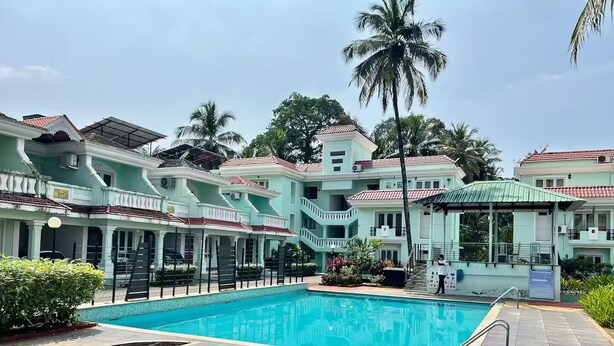 A swimming pool with a surrounding patio area, a covered seating area, and a multi-story building with balconies.