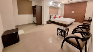 A hotel room with a bed, a desk, a chair, a wardrobe, and a ceiling fan. - Hotel Abhinandan (Bhopal)