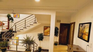 A hotel lobby with a staircase, potted plants, a wooden door, and a painting on the wall. - Hotel Abhinandan (Bhopal)