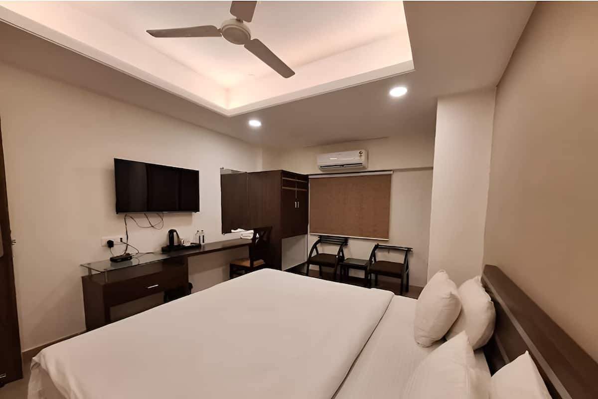 A hotel room with a bed, a desk with a flat-screen TV, a ceiling fan, and an air conditioning unit.