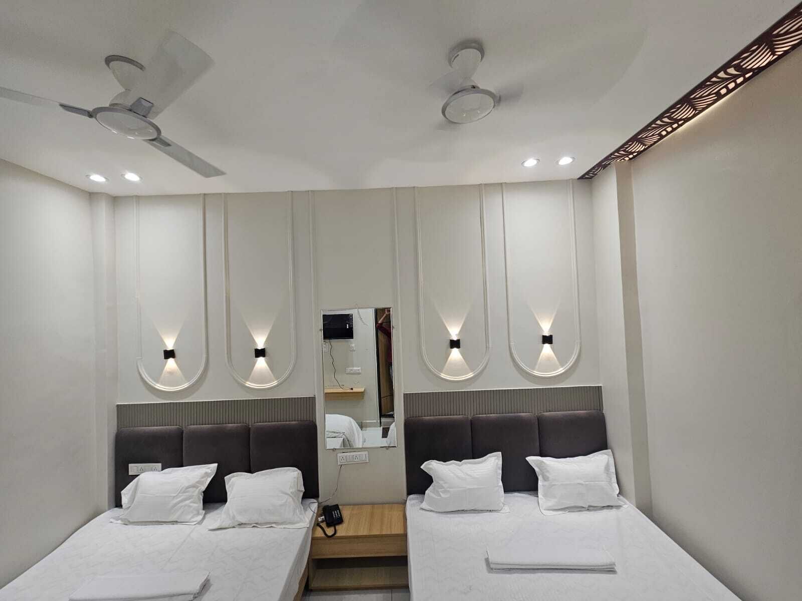 Una habitación de hotel moderna con dos camas, ventilador de techo, iluminación empotrada y un espejo grande.