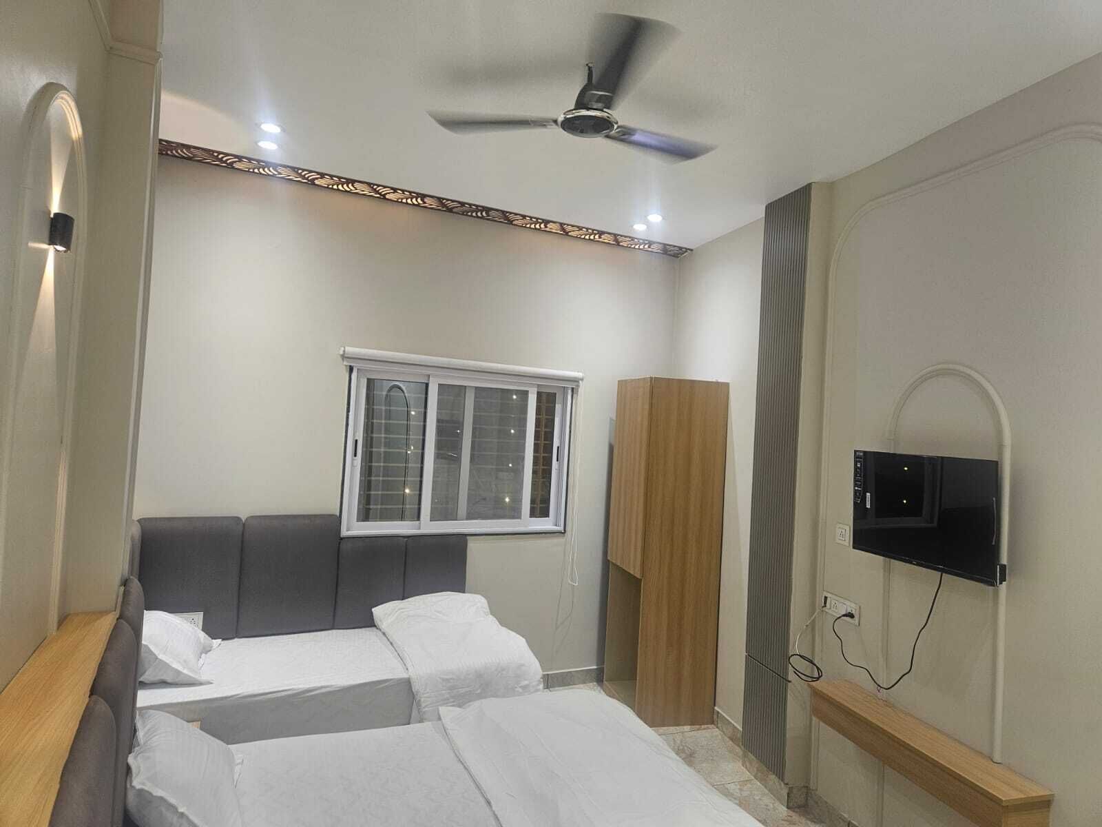 A bedroom with a bed, a wardrobe, a television mounted on the wall, and a ceiling fan.