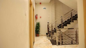 Ein Hotelgang mit Marmorboden, einer Topfpflanze, einem Feuerlöscher und einer Treppe mit Metallgeländern.