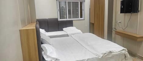 A bedroom with a bed, a window, a TV, and a bedside table.