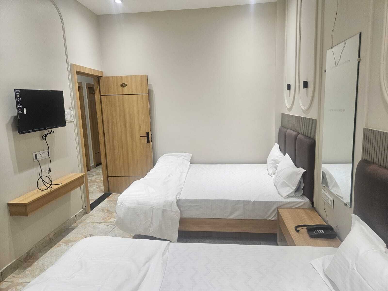 A hotel room with two single beds, a TV, a wooden wardrobe, a bedside table with a phone, and a mirror.