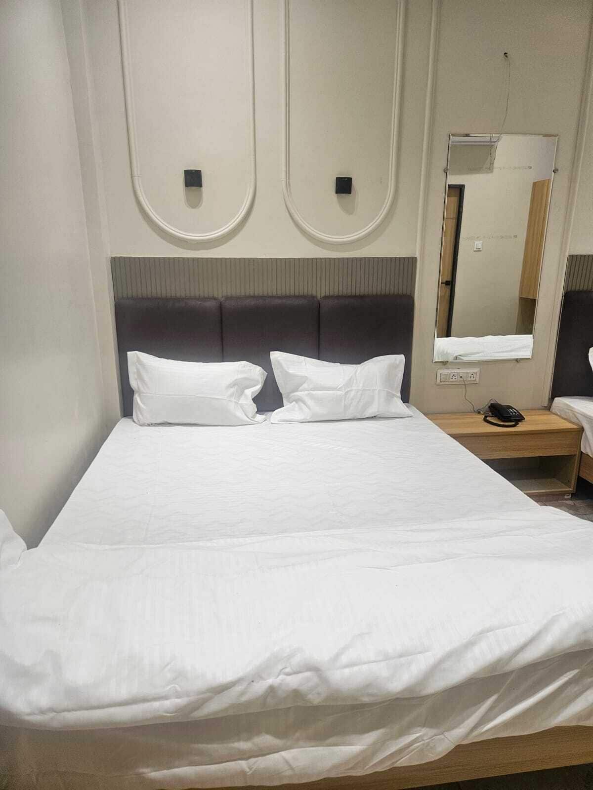 A hotel room with a large bed, a bedside table with a lamp, and a mirror on the wall.