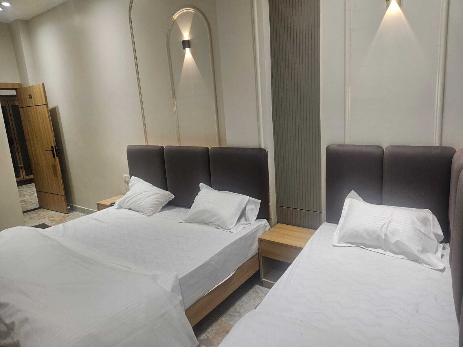 Une chambre d’hôtel moderne avec deux lits, une armoire en bois et un luminaire fixé au mur.