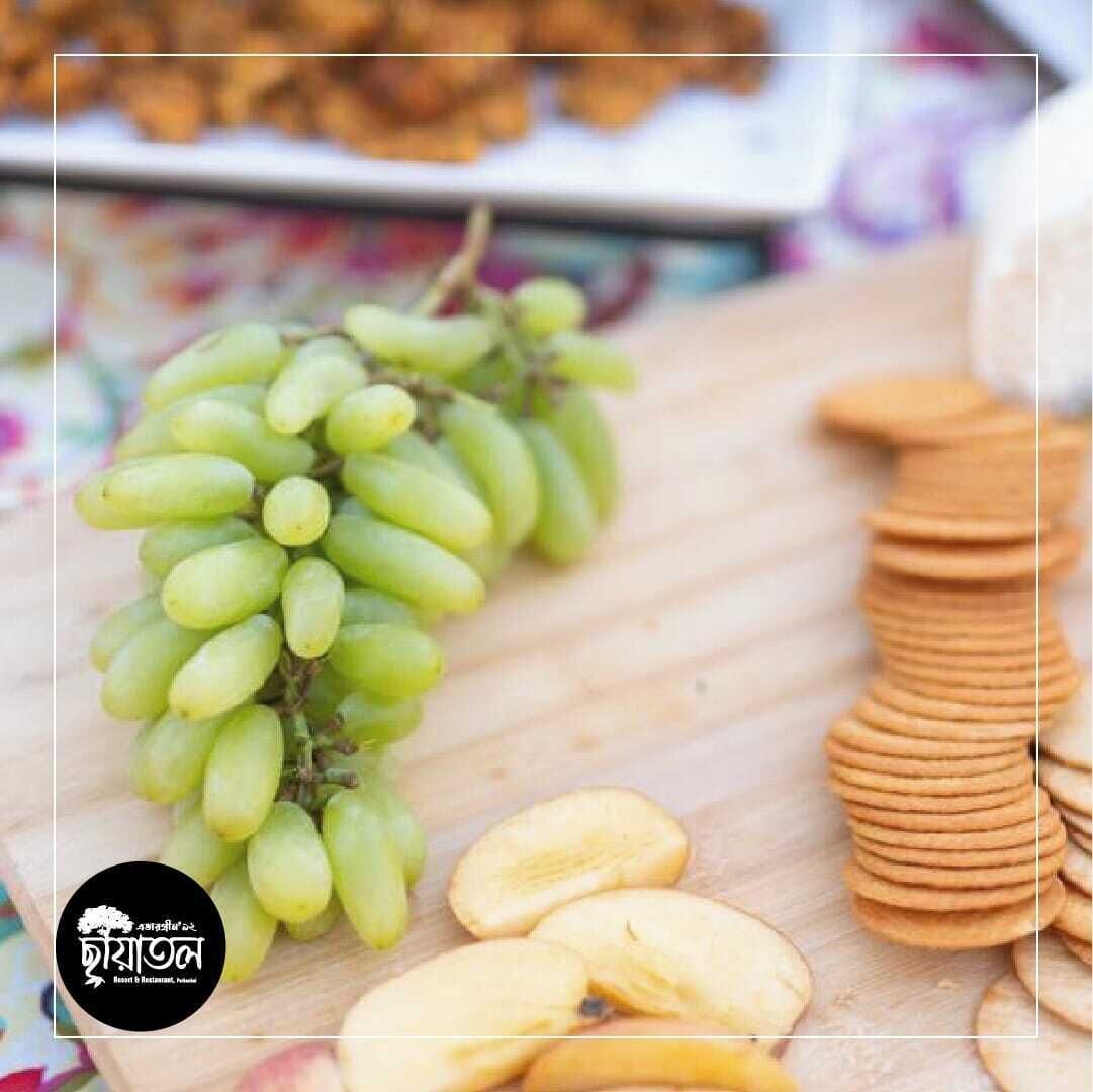 A wooden cutting board with a bunch of green grapes, sliced apples, and stacked cookies.