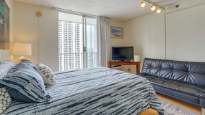 Ein Hotelzimmer mit Bett, Fernseher, Ledersofa und Fenster mit Blick auf die Stadt.