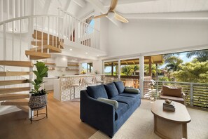 A modern interior with a curved staircase, a dark blue sofa, and a dining area with a view of greenery. - NEW Trendy Surf & Stay Getaway Princeville (Princeville)
