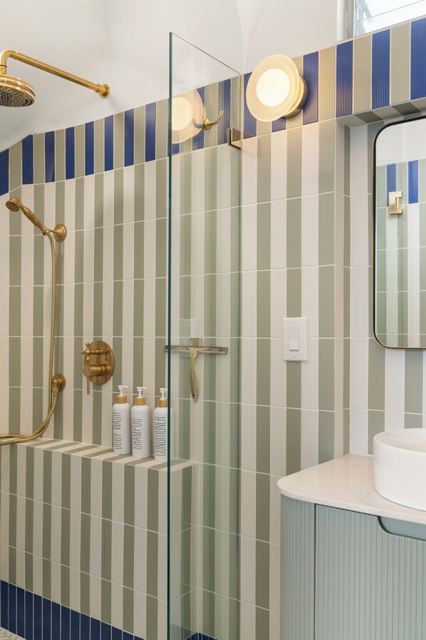 A bathroom with a glass shower enclosure, a white sink, and striped tile walls. - NEW Trendy Surf & Stay Getaway Princeville (Princeville)