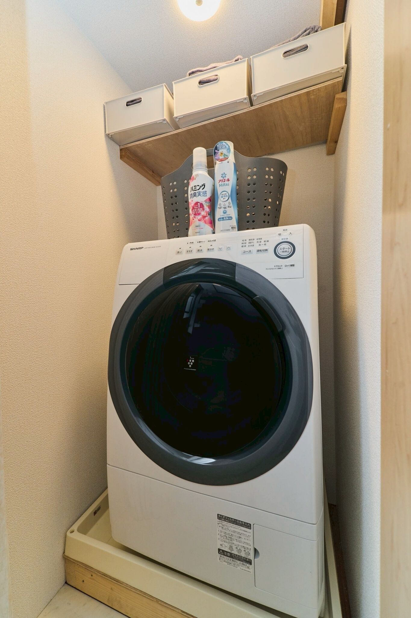 A compact, white front-loading washing machine in a small laundry room with wooden cabinets above.