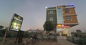 A modern hotel with a sign for Rajwadi Multicuisine Restaurant & Takawyi, a motorcycle parked in front, and a mountainous backdrop. - Hotel Decent Inn (Udaipur)