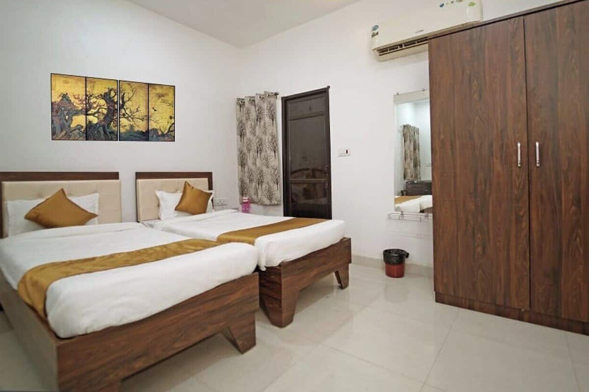 A bedroom with two beds, a wooden wardrobe, a painting on the wall, and a bathroom visible through a door.