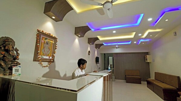 A reception area with a receptionist, a framed religious statue, and modern lighting. - Hotel Decent Inn (Udaipur)
