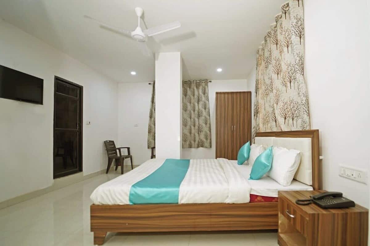 A bedroom with a bed, a wooden nightstand, a ceiling fan, a TV mounted on the wall, and a window with curtains.