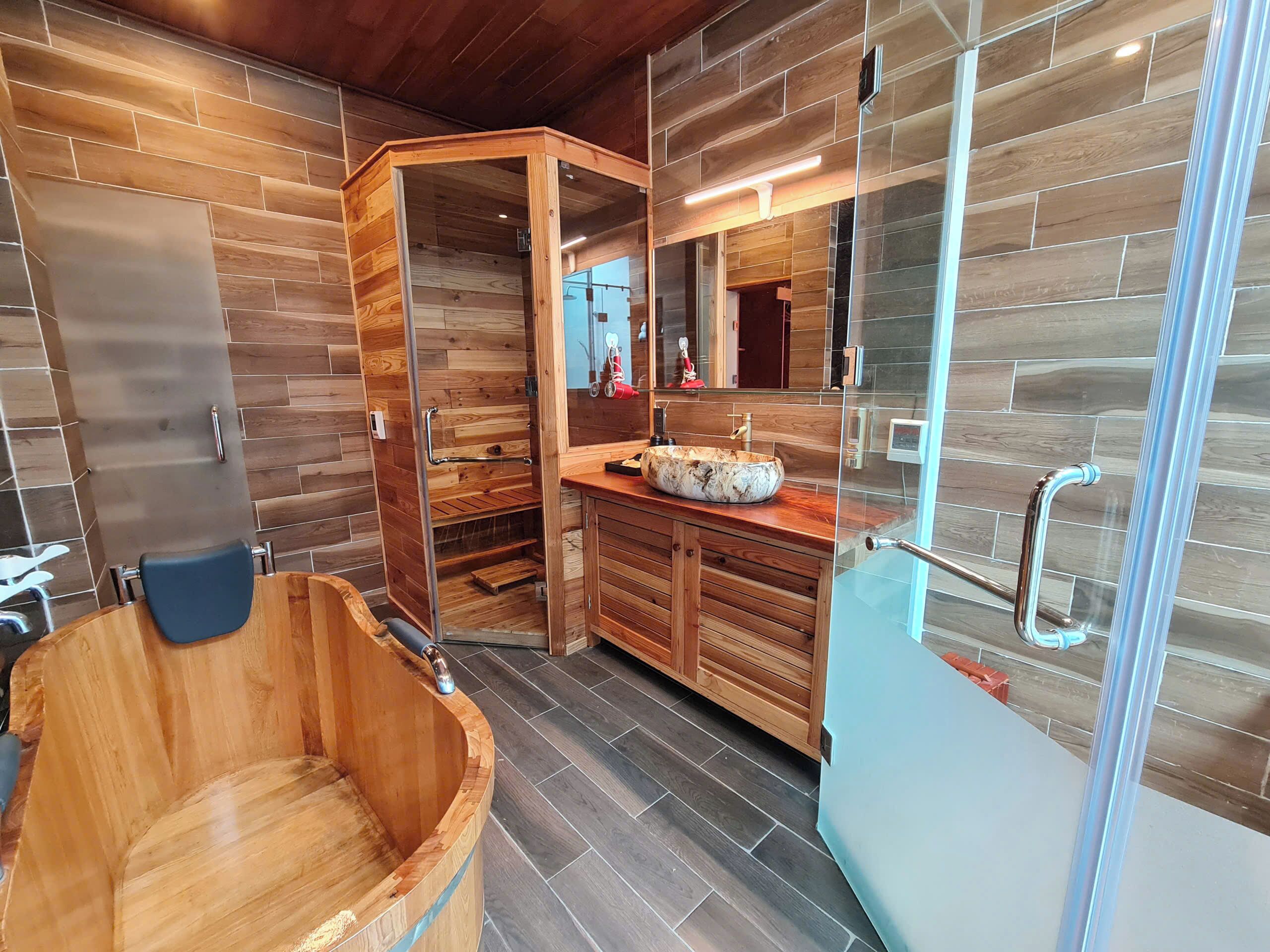 A modern bathroom with a wooden bathtub, a glass shower enclosure, and a wooden vanity with a marble sink.
