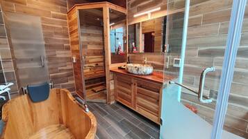 A modern bathroom with a wooden bathtub, a glass shower enclosure, and a wooden vanity with a marble sink.