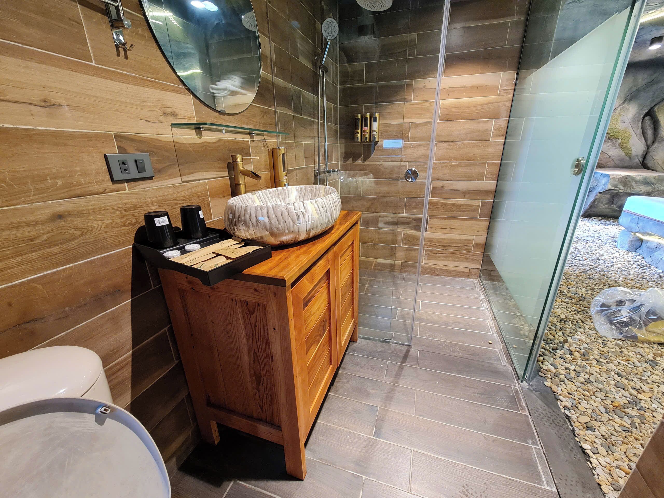 A modern bathroom with a wooden vanity, a large mirror, and a glass shower enclosure.