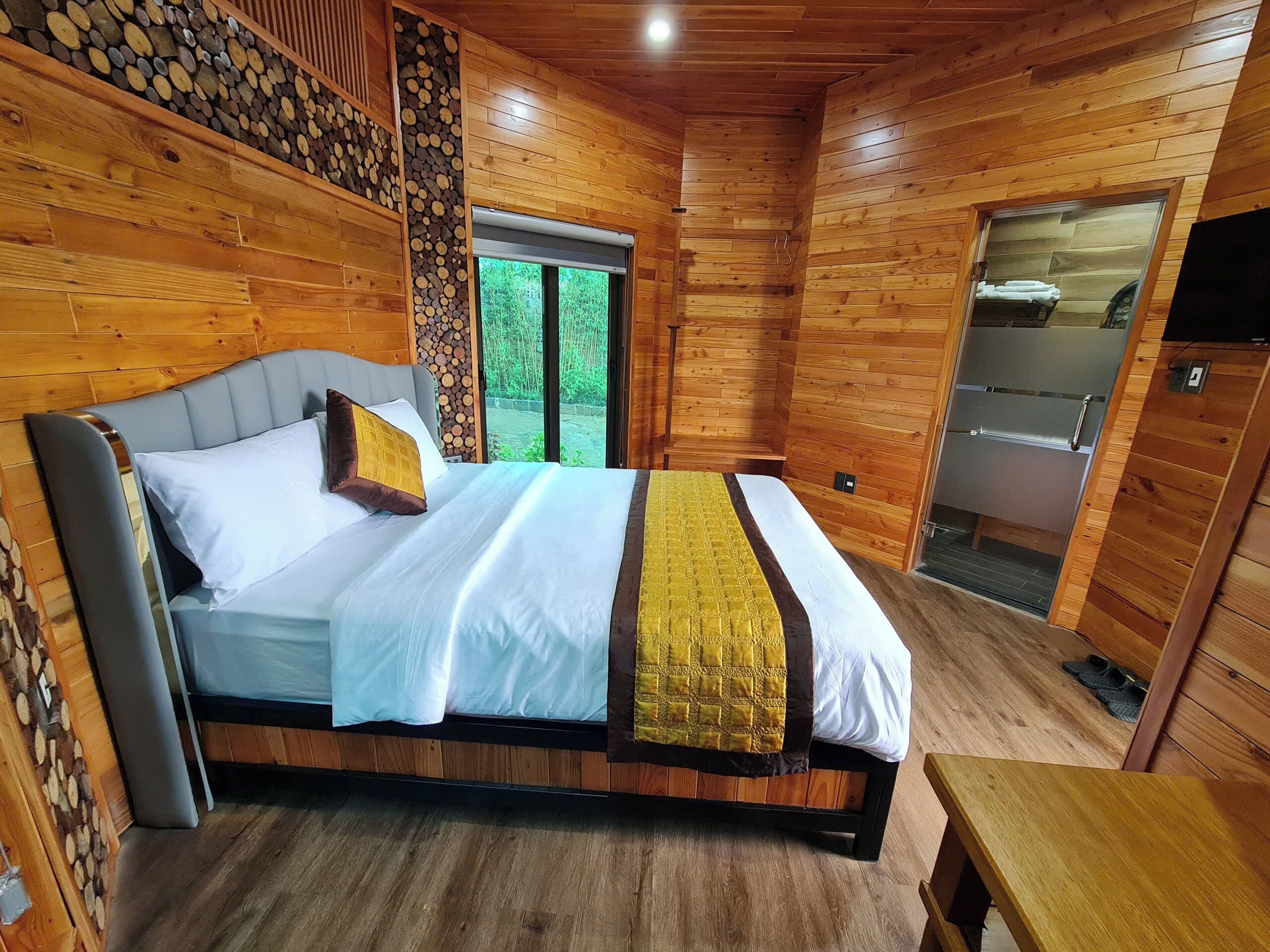A wooden-paneled bedroom with a bed, a window, and a door leading to a bathroom.