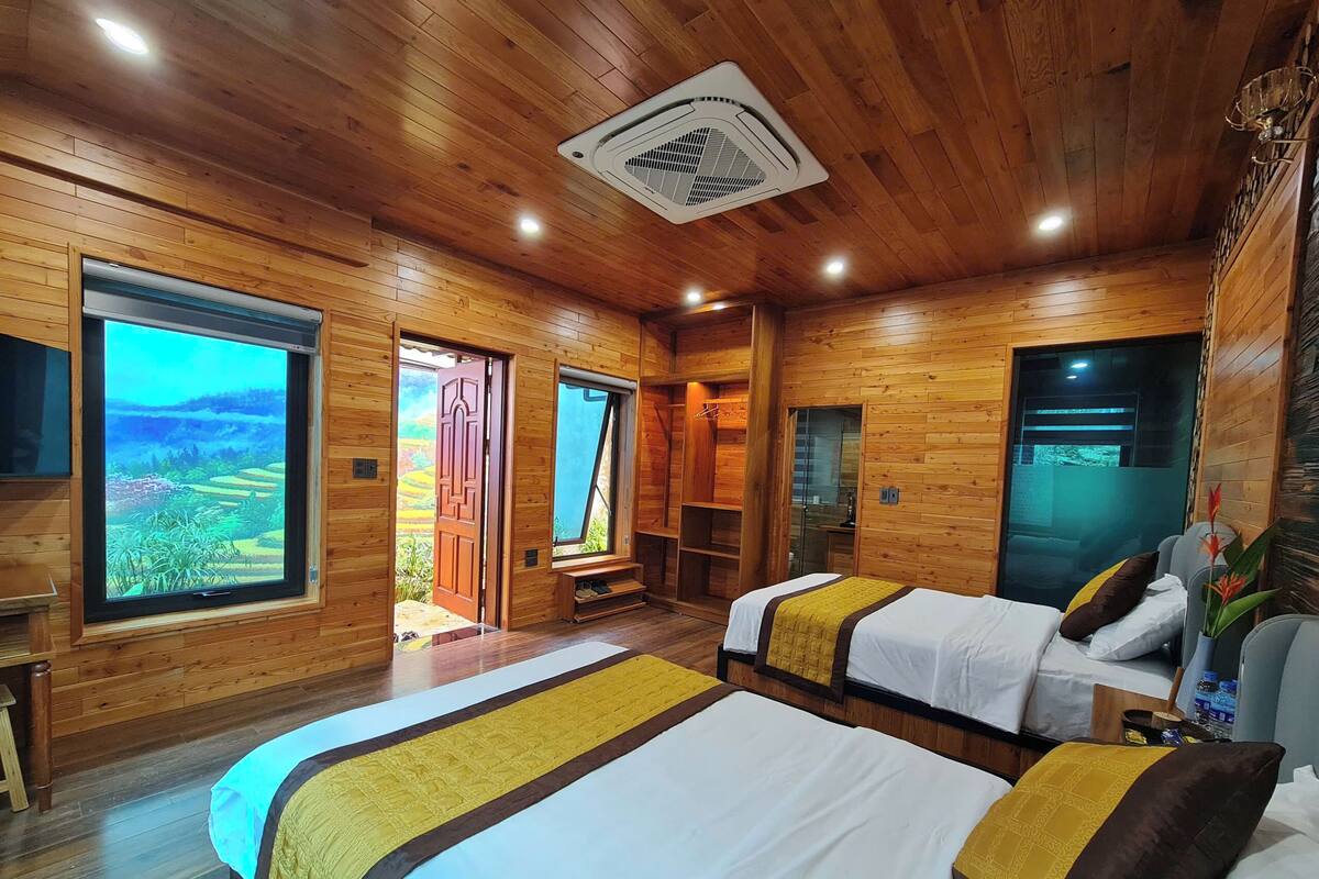 Una habitación tipo cabaña de madera con dos camas, un ventanal con vistas al paisaje y un ventilador de techo.