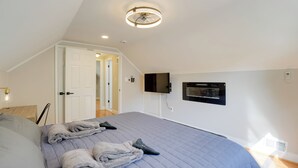 A bedroom with a bed, a ceiling fan, a TV, and a door leading to another room.