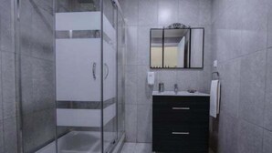 A modern bathroom with a glass-enclosed shower, a black vanity with a mirror, and grey tiled walls. - GuestReady - Casa das Arcadas - Room 10 (Ponta Delgada)