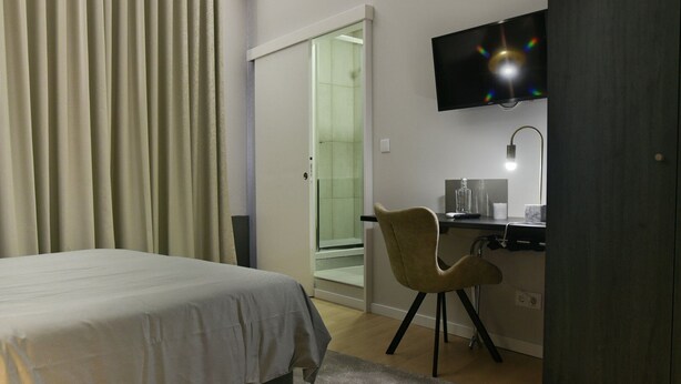 A hotel room with a bed, a desk with a chair, a television, and a bathroom with a glass shower. - GuestReady - Casa das Arcadas - Room 10 (Ponta Delgada)