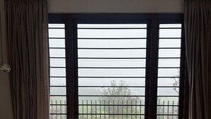 Une chambre avec un grand lit, une vue sur un balcon agrémenté d’une balustrade et des rideaux aux fenêtres.