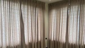 Une pièce spacieuse avec un sol carrelé de couleur beige et de grandes rideaux beiges qui recouvrent les fenêtres.