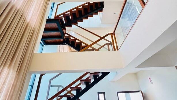 Un intérieur à plusieurs niveaux, relié par un escalier, agrémenté d’un lustre moderne et doté de grandes fenêtres laissant entrer la lumière naturelle.