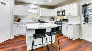 Une cuisine moderne avec des meubles blancs, un îlot central doté de tabourets, un four encastré et un four à micro-ondes.