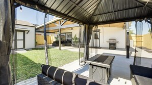 Un espace extérieur aménagé en terrasse, avec un coin salon couvert, un barbecue et une balançoire.
